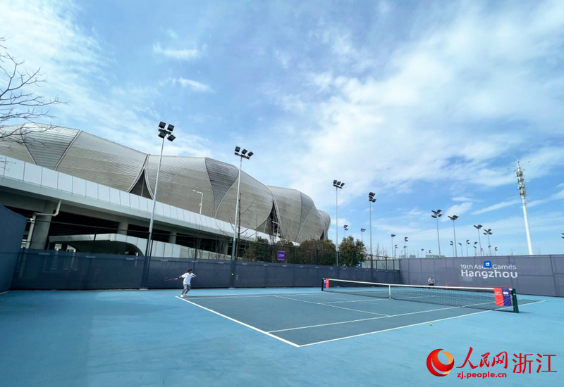 網球場上，市民“激戰正酣”，球場背后就是杭州亞運會開幕式舉辦地“大蓮花”。人民網記者 王麗瑋攝
