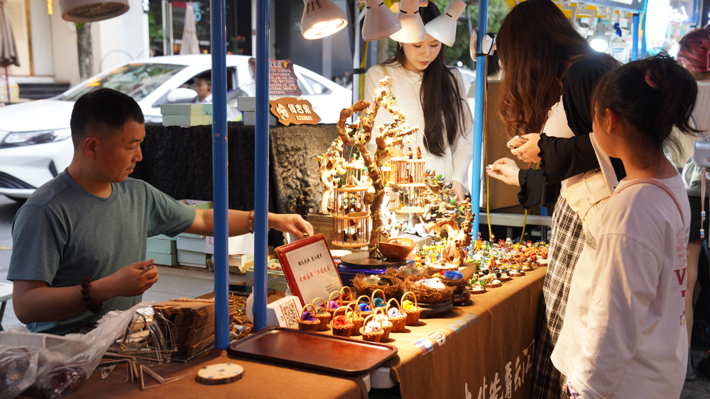 杭州市拱墅區武林夜市的一家手工藝品攤位前，游客正在選購商品。程欣攝